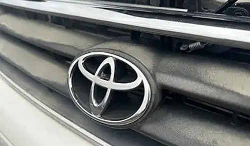 Close-up of a silver Toyota emblem on the front grille of a dusty car