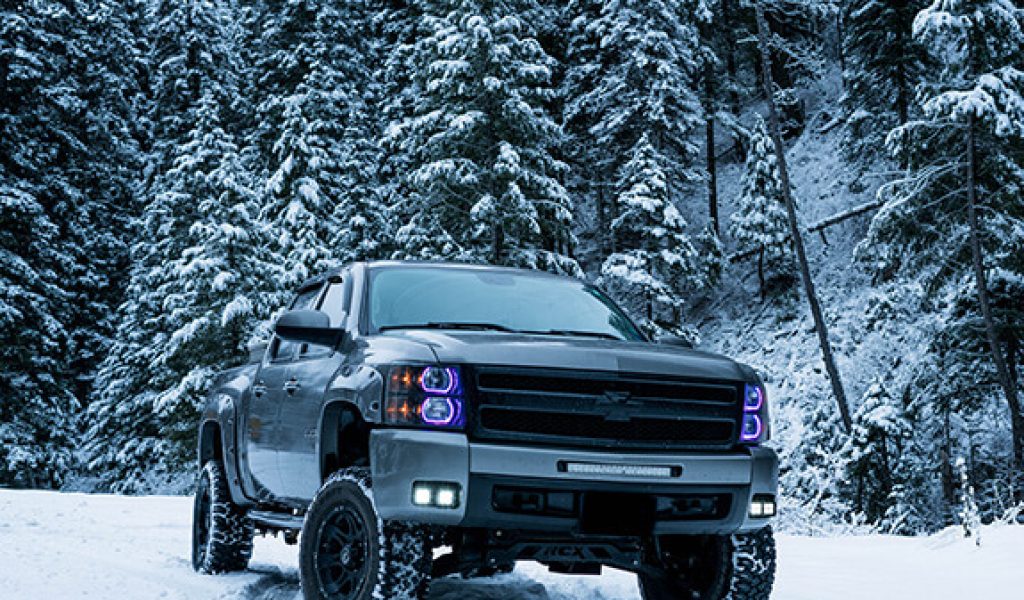Old Chevy Silverado driving through the snow with ever green tress in the background